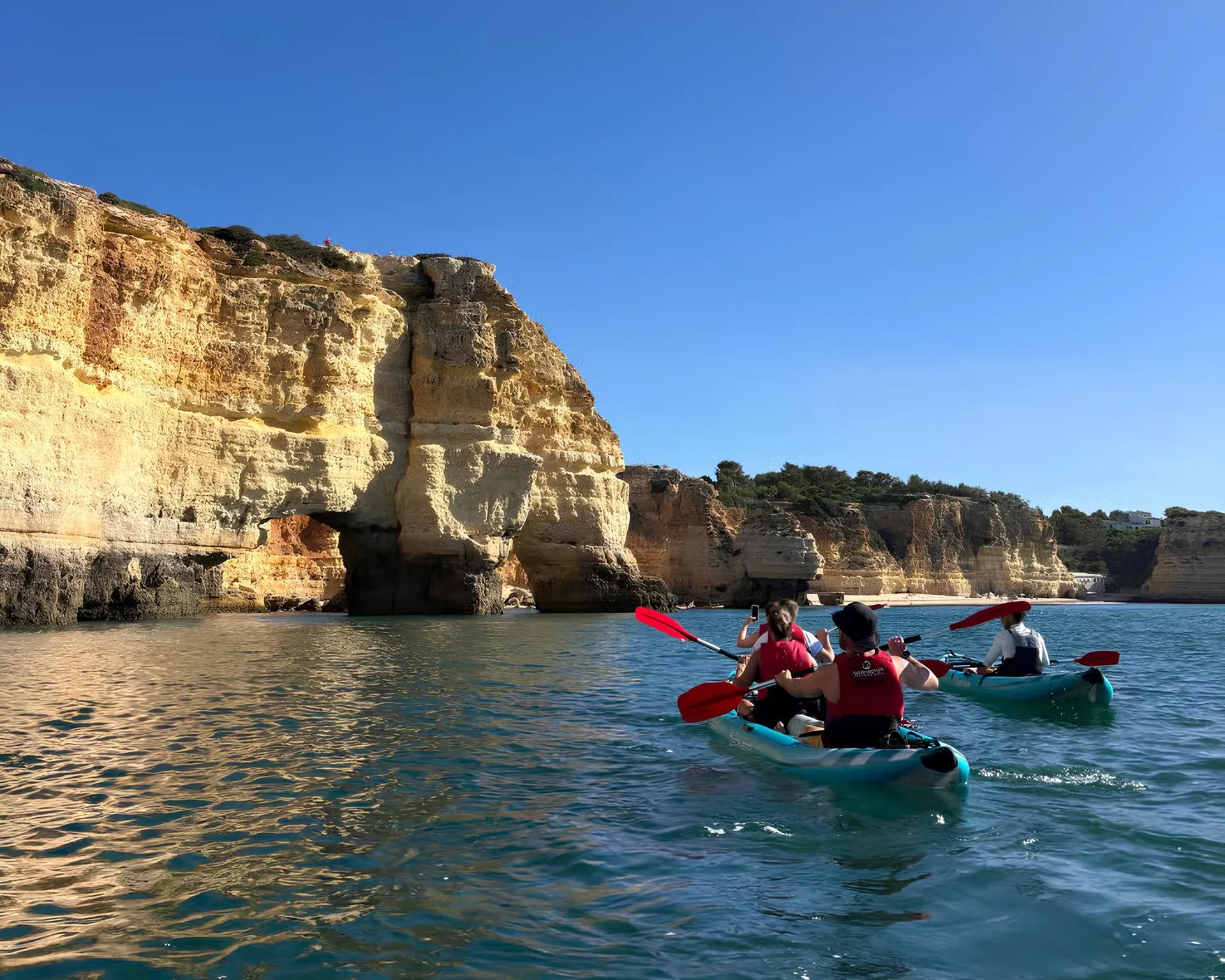 Couple kayaking along golden limestone cliffs of Benagil, Algarve